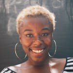 Portrait of a cheerful Black woman with afro hairstyle and hoop earrings smiling in natural light.